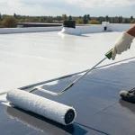 Worker applying flat roof sealant with a roller for a roof repair.