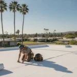 Professional roofer inspecting a flat roof membrane on a Southern California home with palm trees in the background